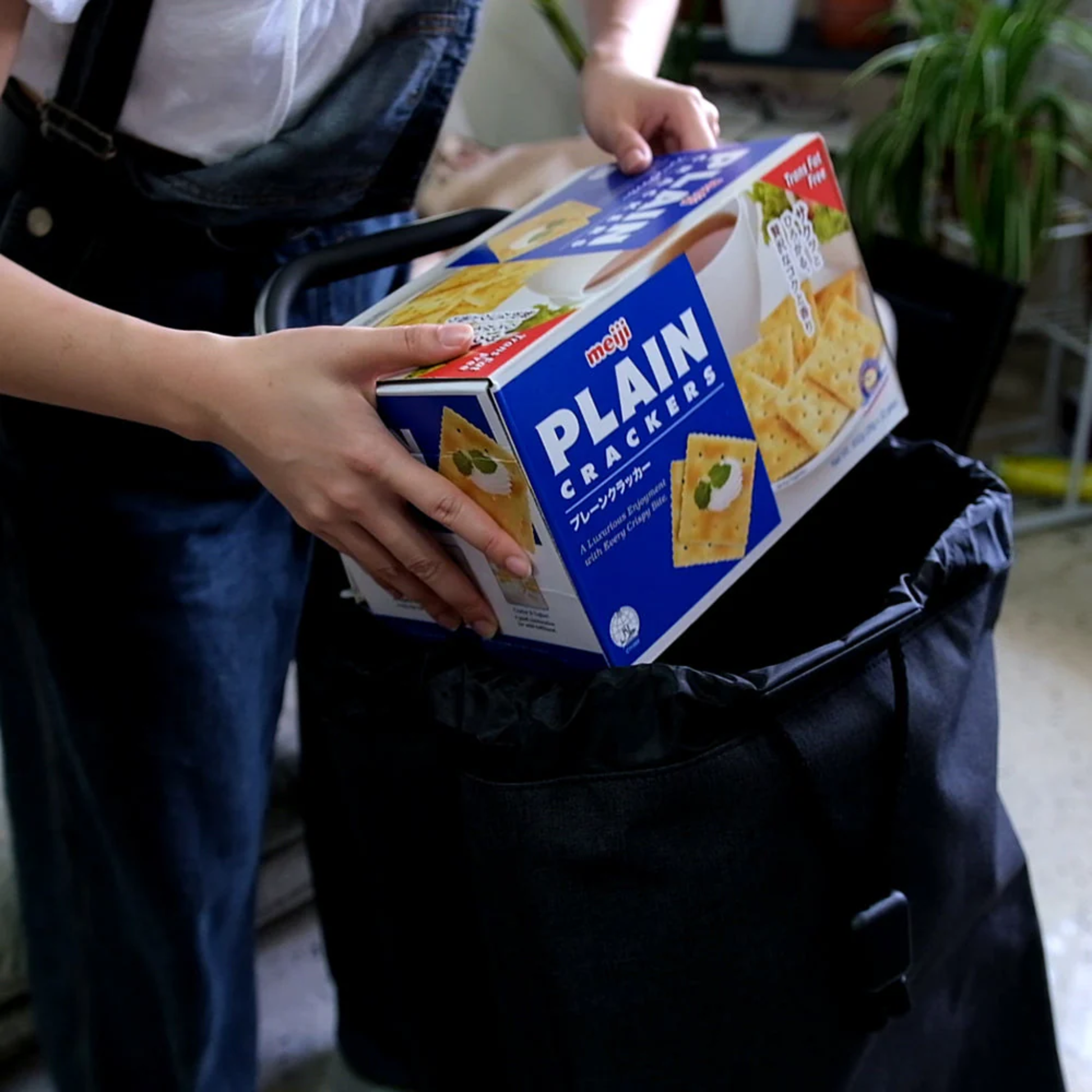 Person loading a large box of plain crackers into a black Rolser tweed grocery shopping trolley, showing spacious 40L bag capacity.