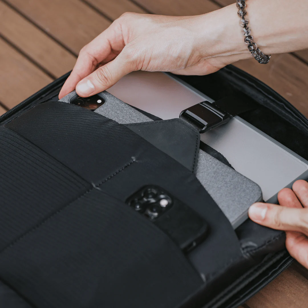 Hands placing a tablet and smartphone into padded compartments of a black tech organizer pouch, showing secure storage for electronic devices and accessories.