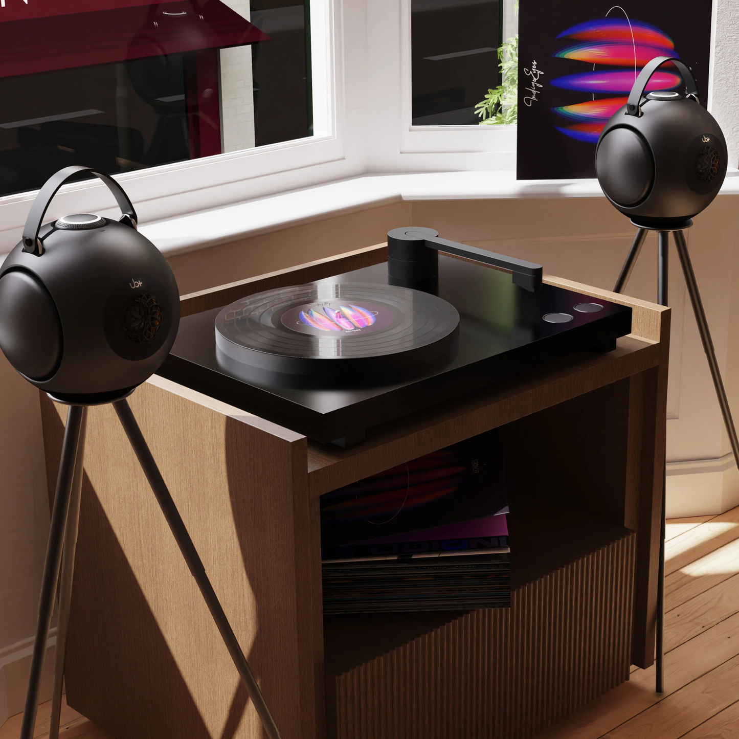 Pair of UB+ DB1 Doublebass portable speakers in metallic grey, set on tripod stands beside a modern turntable in a sunlit corner room with large windows.