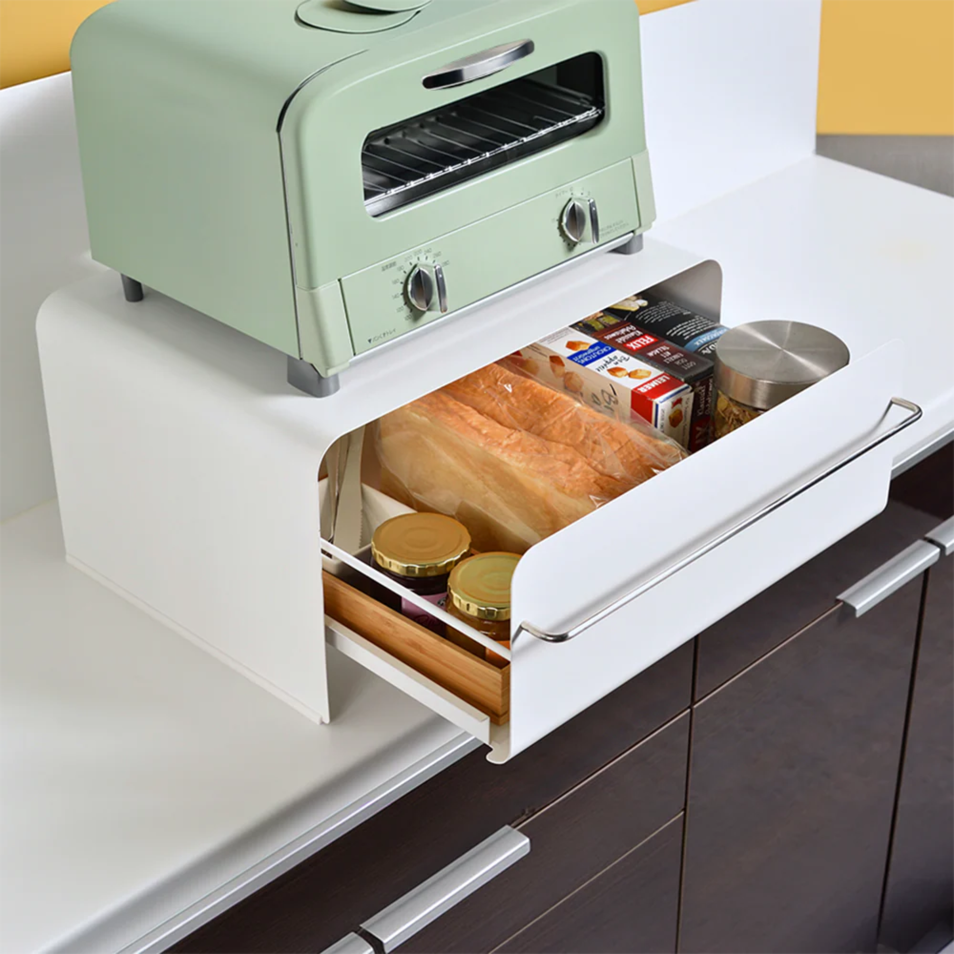 UtaU Bread Drawer in white under retro mint green toaster, open kitchen storage drawer neatly organising bread, snacks and jars on countertop.