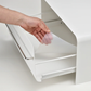 Hand lifting removable tray inside UtaU Bread Drawer in white, showing easy-to-clean interior and adjustable storage base.