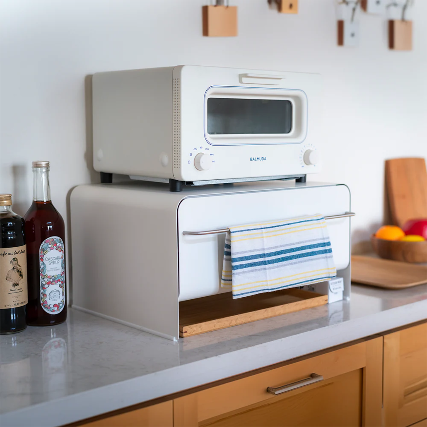 UtaU Bread Drawer in white on kitchen counter, used as stand for Balmuda toaster with striped dish towel hanging from metal bar in modern home.