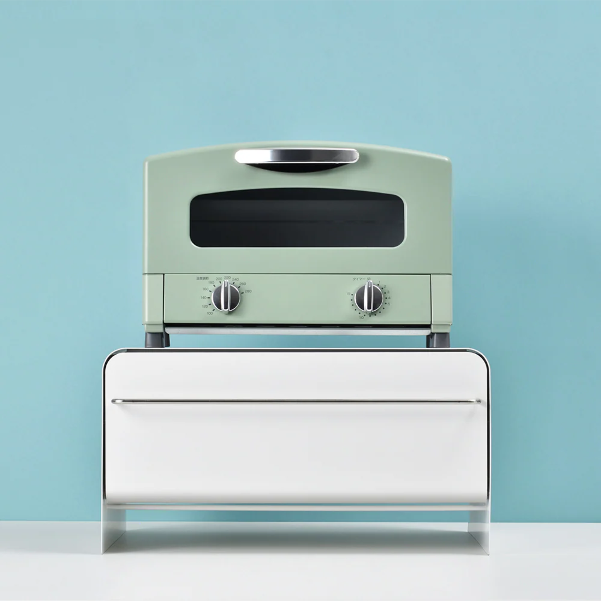 UtaU Bread Drawer in white used as countertop stand, minimalist bread storage box with retro mint green toaster on top against blue wall.