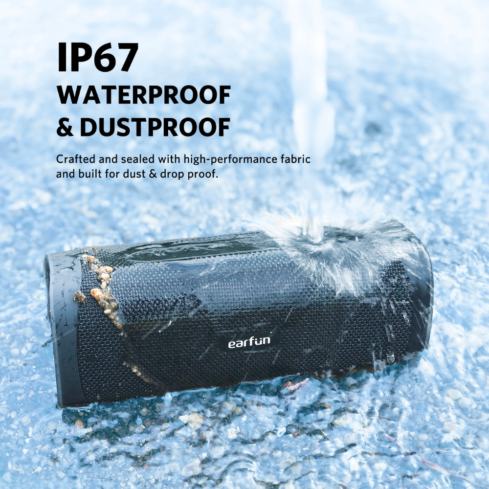 EarFun UBOOM L Bluetooth speaker outdoors on wet gravel, being splashed with water to demonstrate IP67 waterproof and dustproof durability