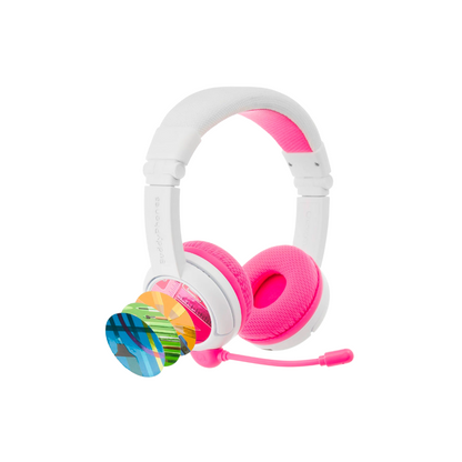White and pink over-ear kids’ headphones with a pink detachable boom microphone, shown with four colorful interchangeable decorative discs fanned out beside the earcup